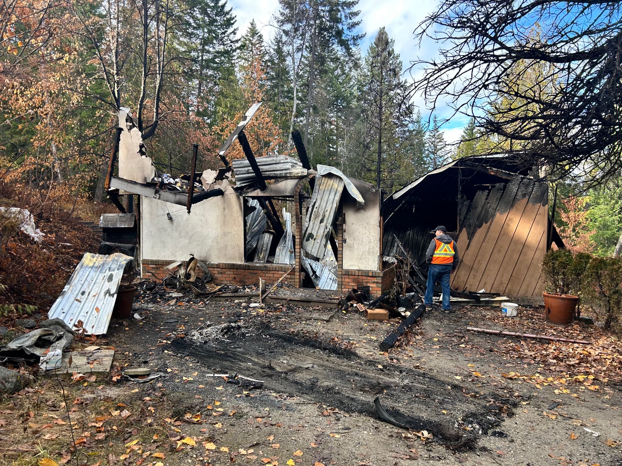 A worker in a safety vest inspects the charred remains of a fire-destroyed building.
